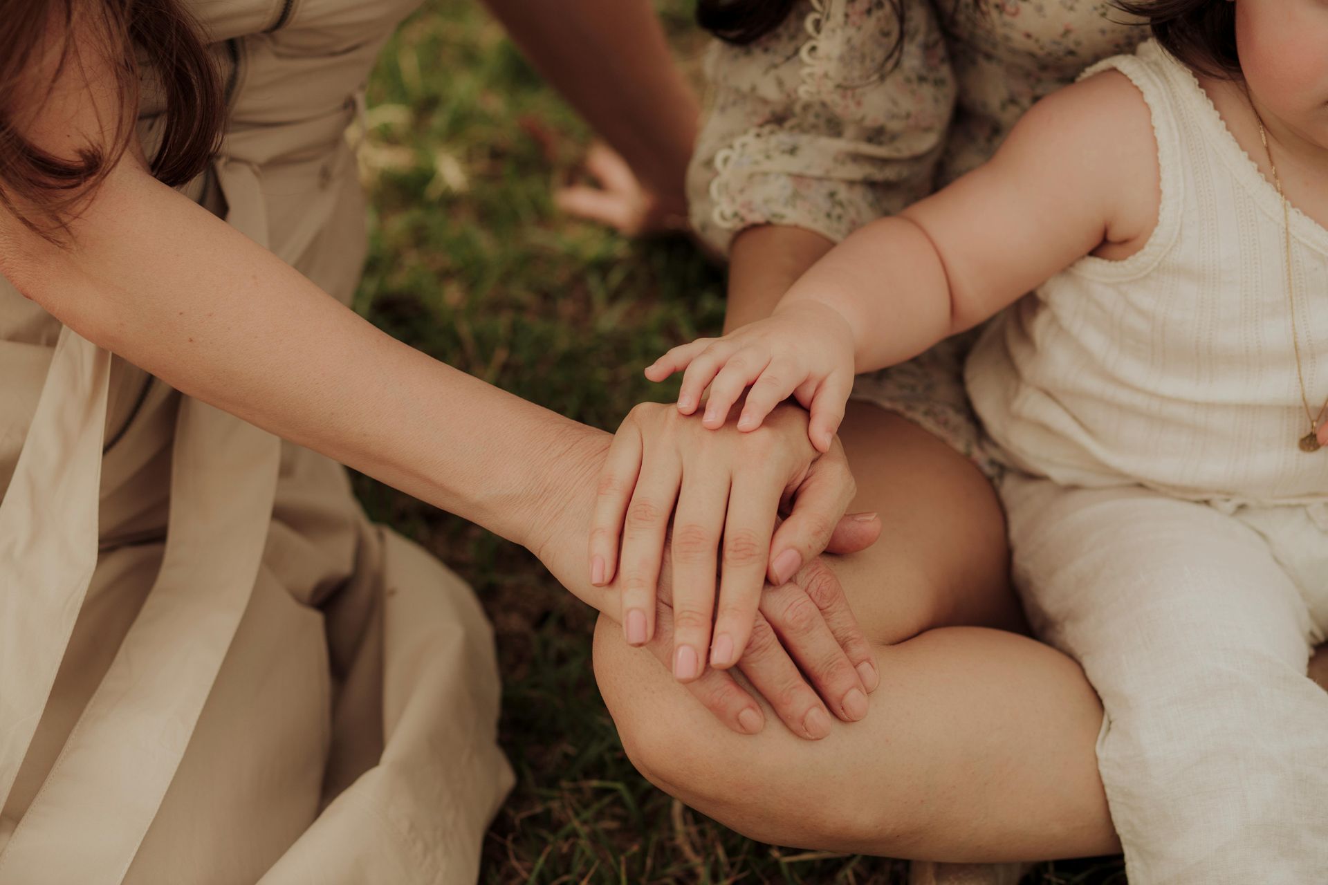 A woman and two children are sitting on the grass holding hands.