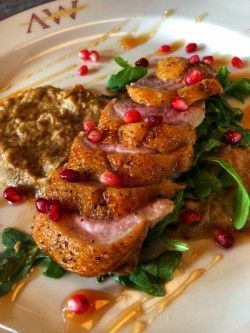 A white plate topped with meat , vegetables and pomegranate seeds.