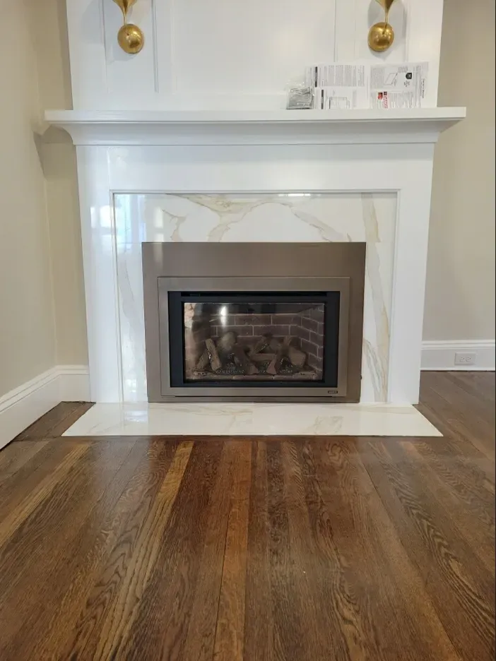 Fireplace with white marble surround, gray metal firebox, and wooden floor.