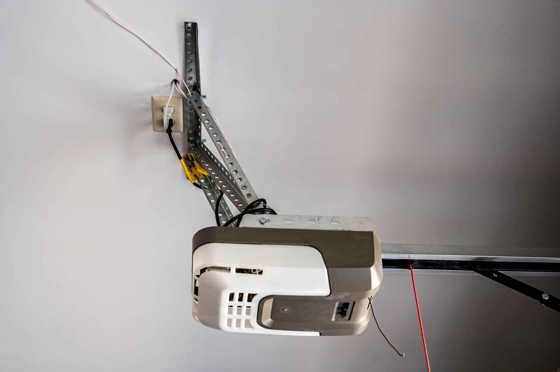 Garage door opener mounted on a ceiling track with exposed wiring and electrical connection.