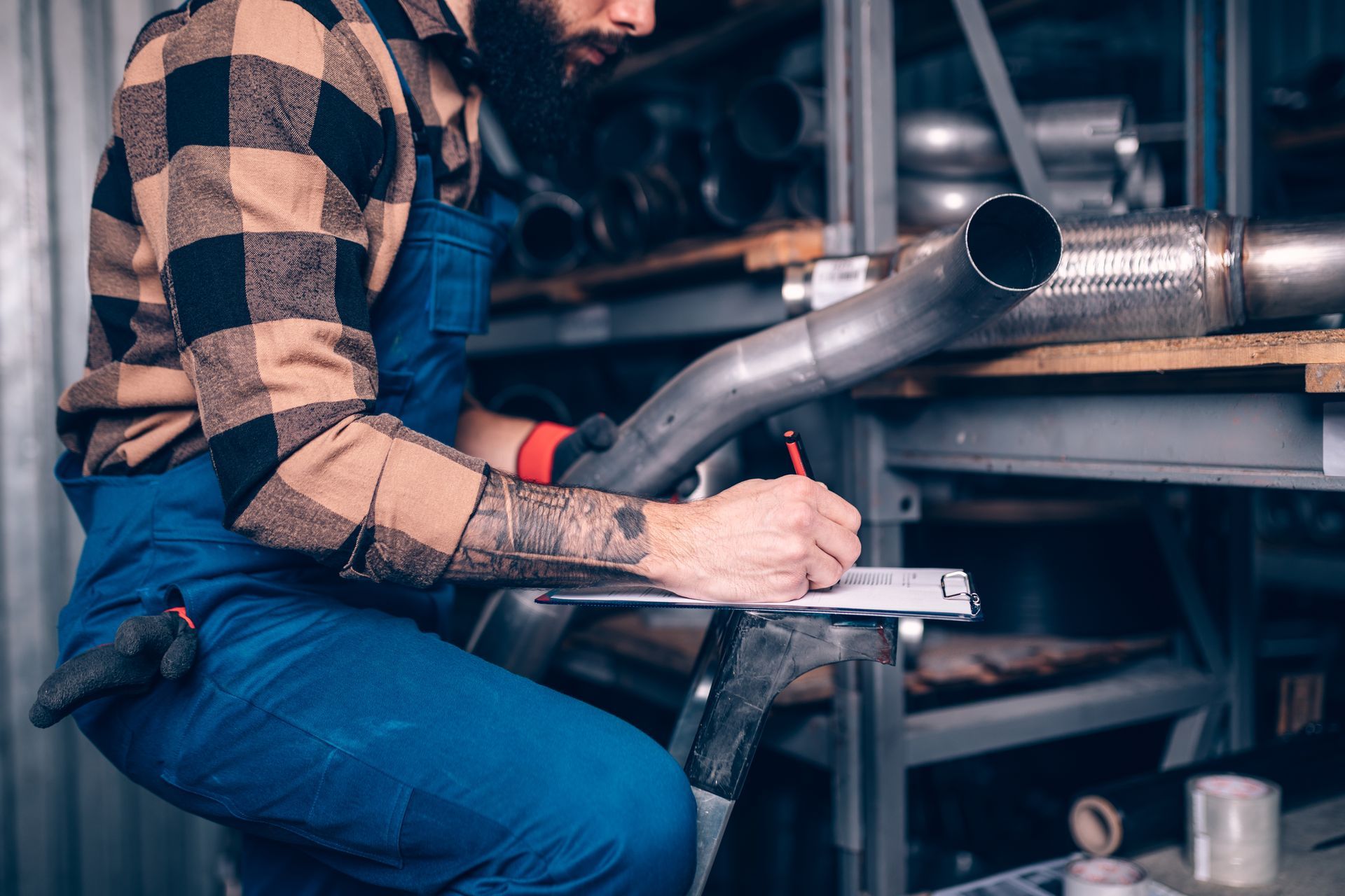 Technician inspecting metal pipes and writing notes during commercial garage repair service check.