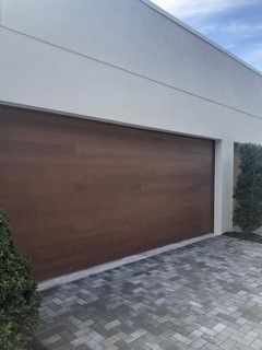 A large wooden garage door is sitting next to a brick driveway.