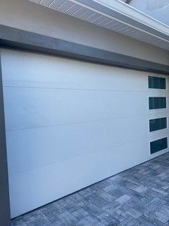 A white garage door with green windows is sitting on top of a brick driveway.