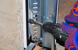 A person is using a drill to fix a garage door.