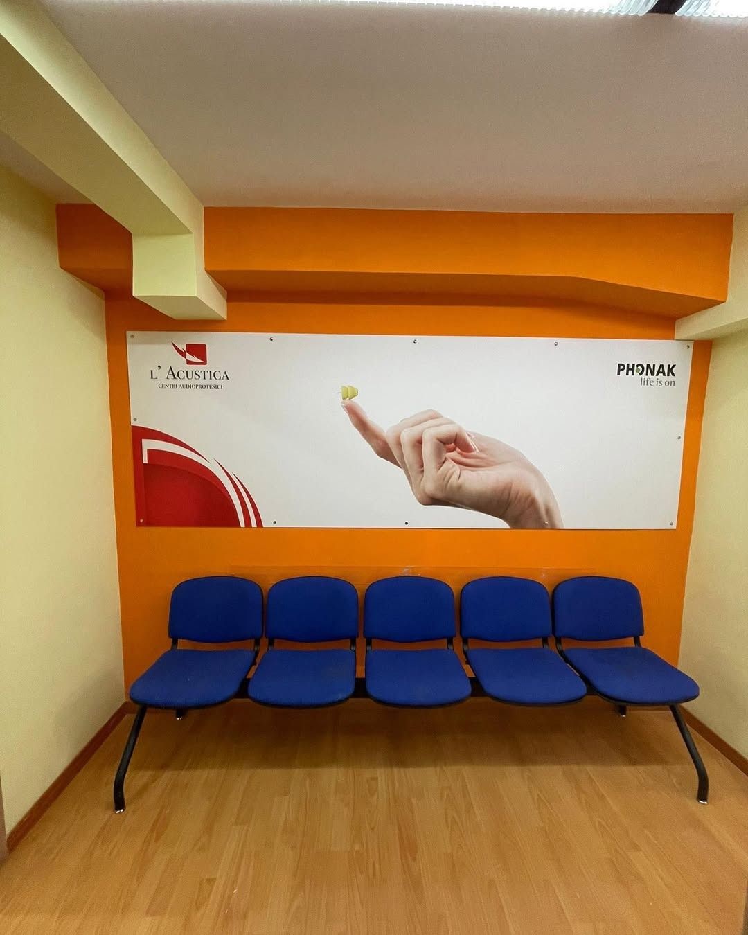 Una sala d'attesa con sedie blu e una parete arancione