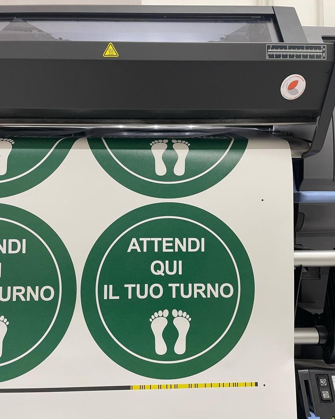 A printer is printing stickers that say attendi qui il tuo turno