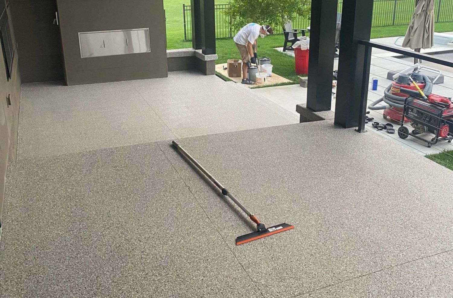 A man is standing on a patio with a broom.