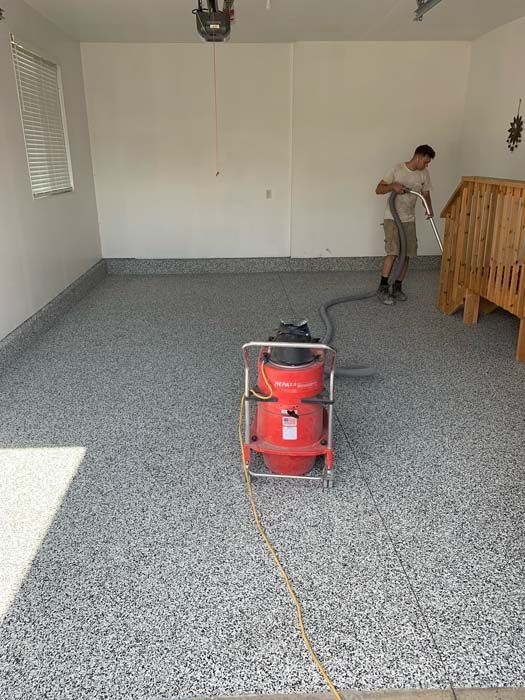 A man is using a vacuum cleaner to clean a garage floor.