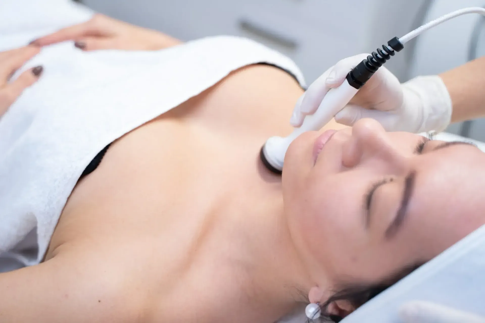 Person receiving a facial peel treatment. A gloved hand applies a liquid from a brush to the forehead.