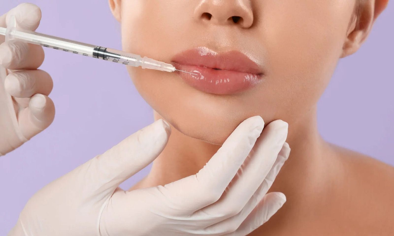 Lips being injected with filler, hands in gloves, lavender background.