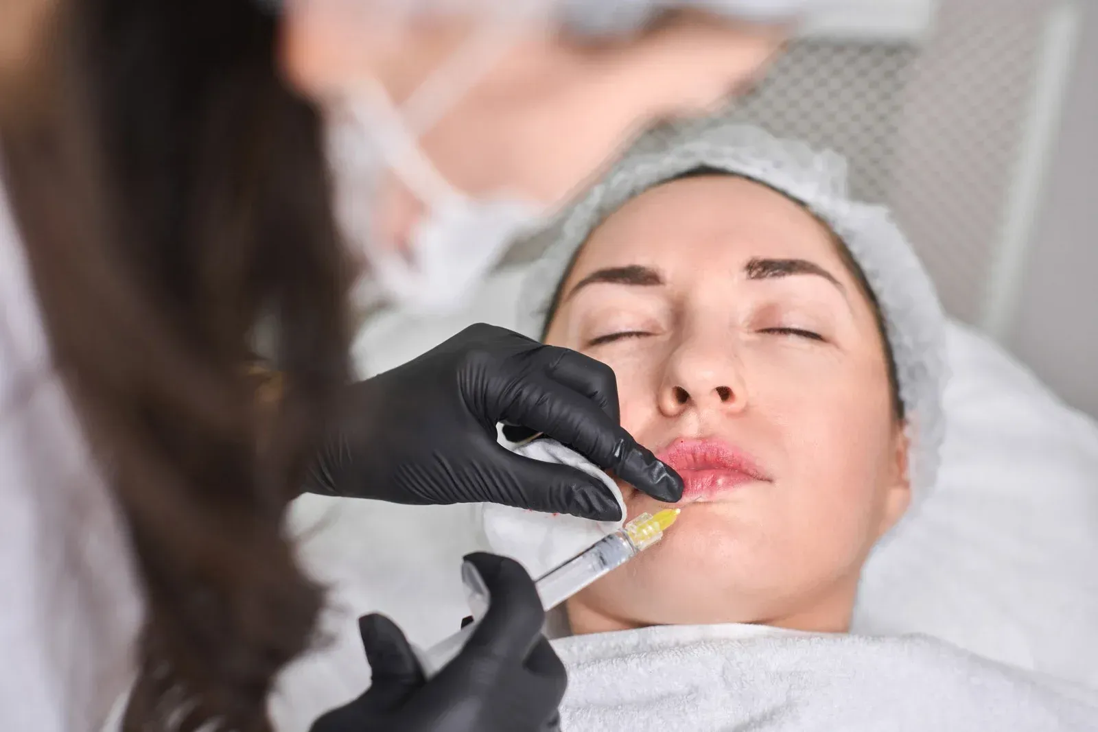 Person receiving lip filler injection in a medical setting; close-up view.