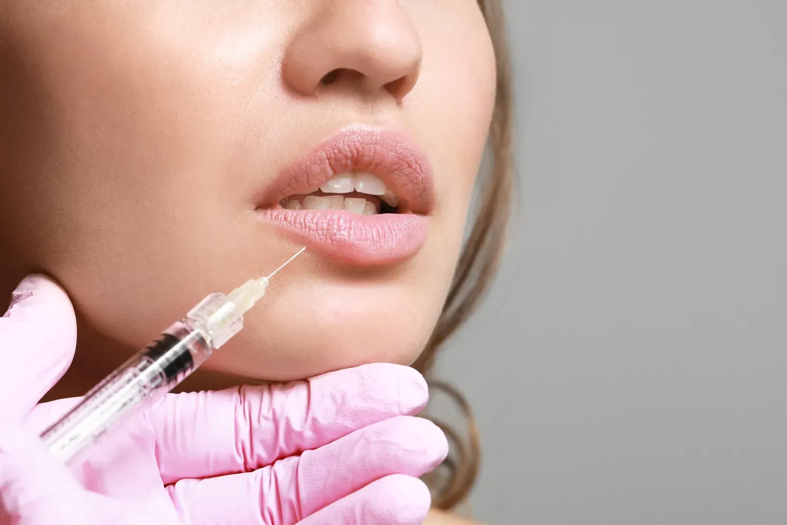 Lip filler injection: Hand in pink glove injecting lip with syringe.