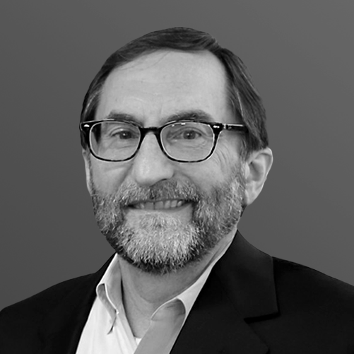 Man with glasses and beard smiling, wearing a blazer.