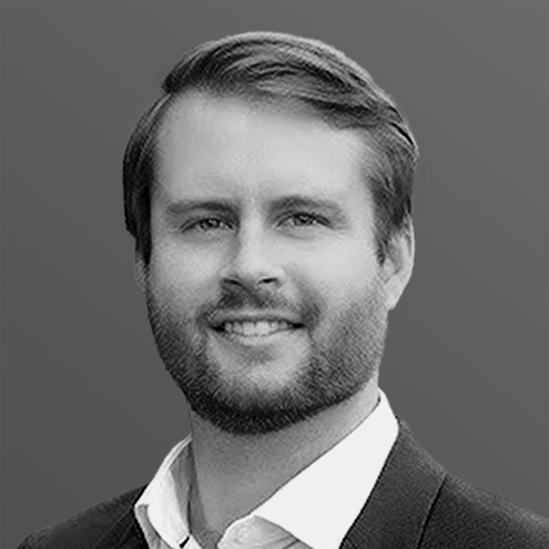 A grayscale headshot of a smiling man in a suit jacket and collared shirt.