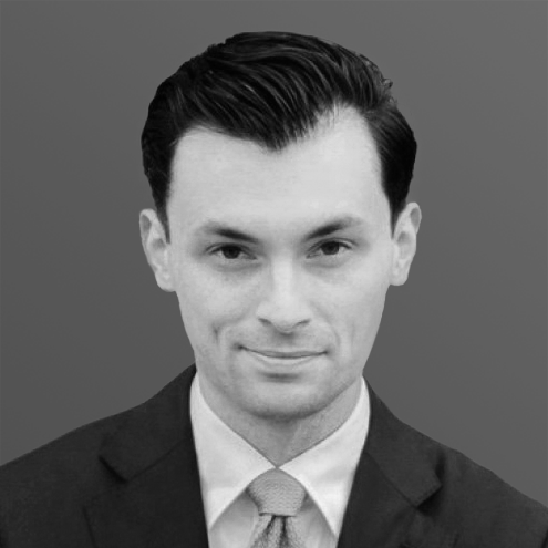 A man in a suit, looking at the camera with a neutral expression, in a grayscale photo.