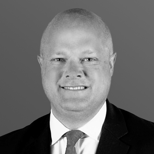 Bald man in suit and tie smiling at the camera. Black and white headshot.