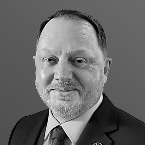 A grayscale portrait of a smiling man in a suit and tie with a full beard.