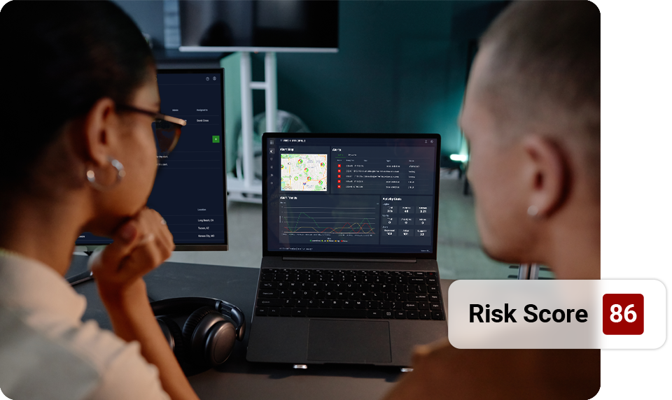 Two people reviewing a laptop with a risk score of 86 displayed, likely analyzing data.
