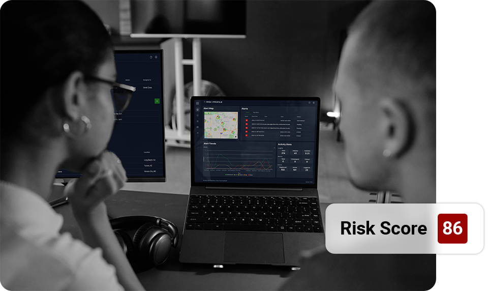Two people reviewing a laptop with a risk score of 86 displayed, likely analyzing data.