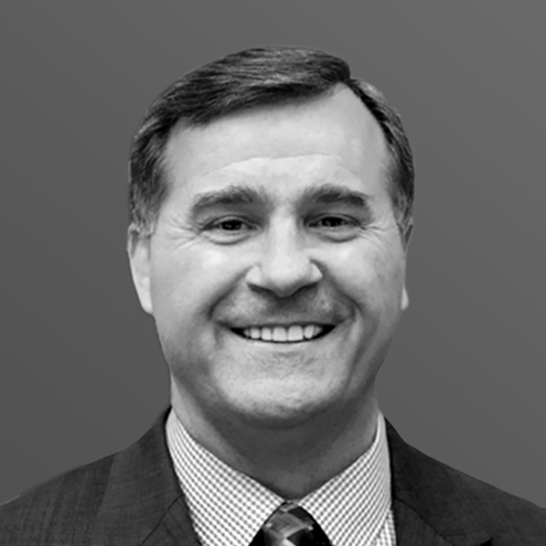 Smiling man in a suit and tie. Black and white headshot against a gray background.