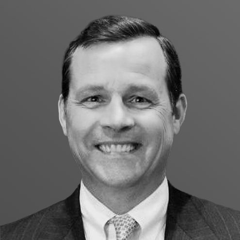 A grayscale headshot of a smiling man in a suit jacket and collared shirt.