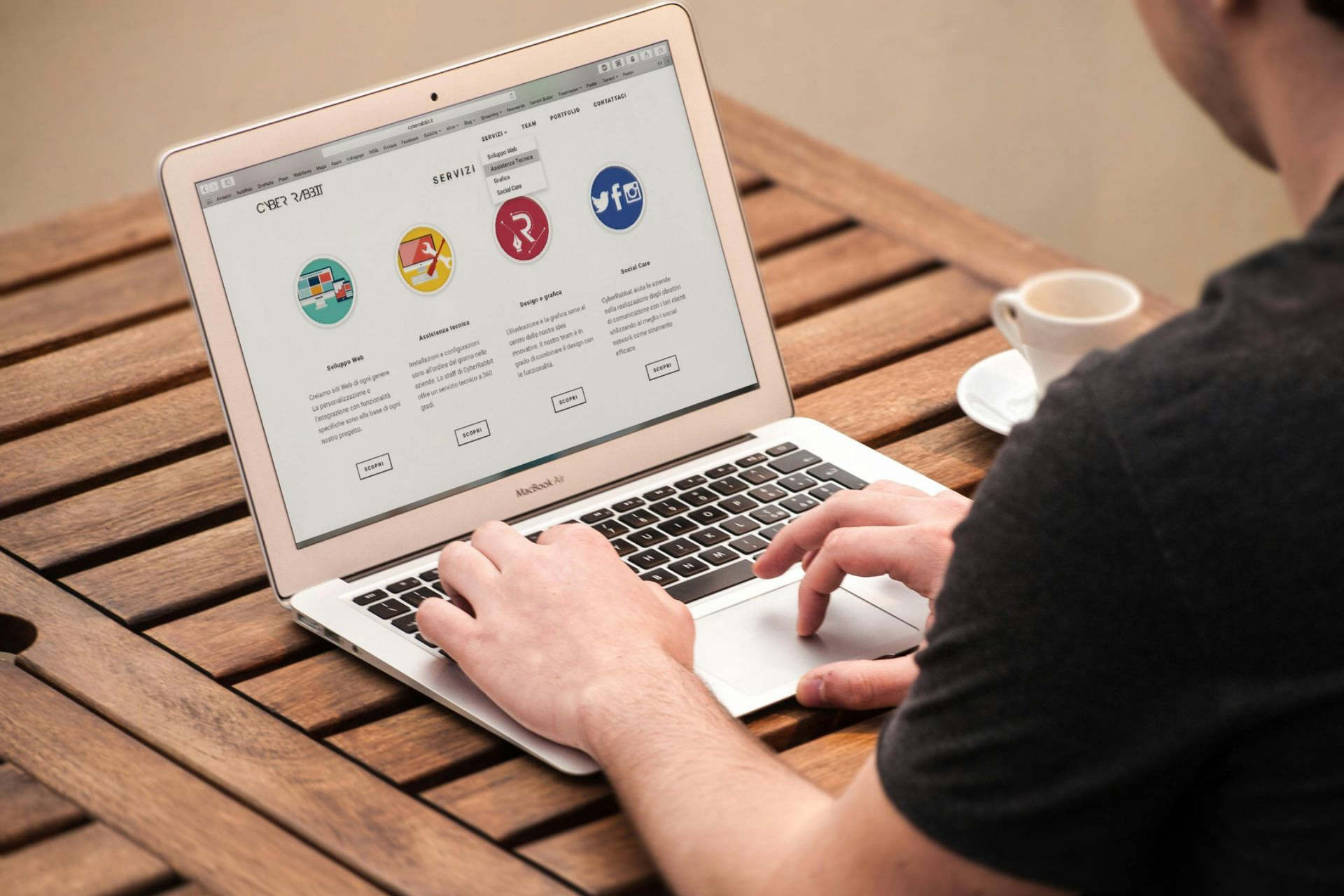 Man using a MacBook at an outdoor table with a coffee cup nearby.
