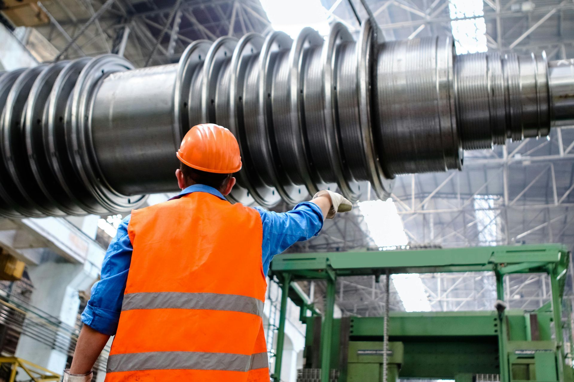 Worker in orange safety vest inspects large metal turbine. Industrial setting.