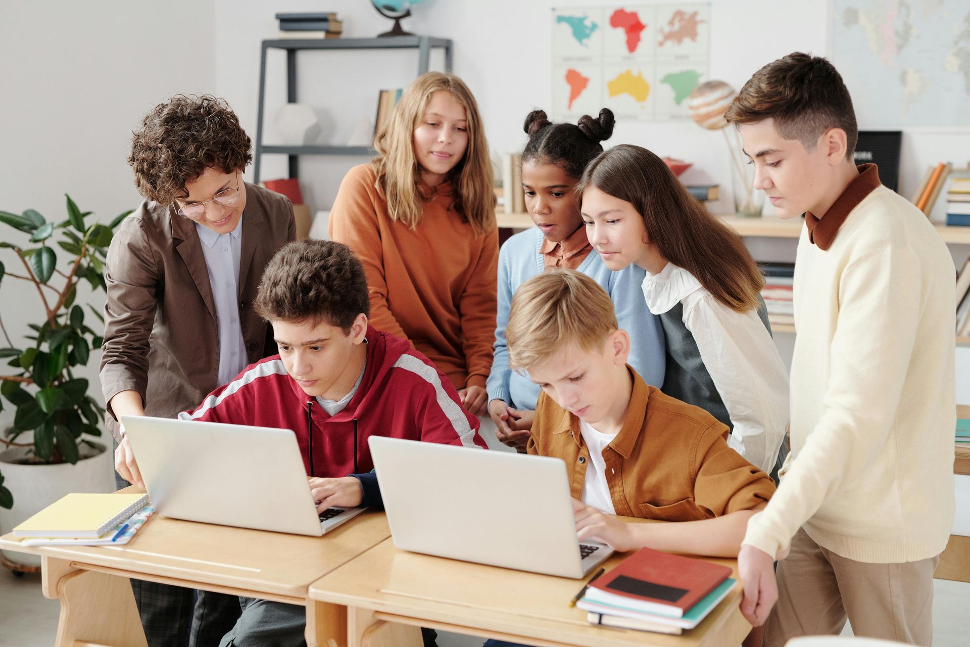 Group of students huddled around two laptops in a classroom, focused and working.