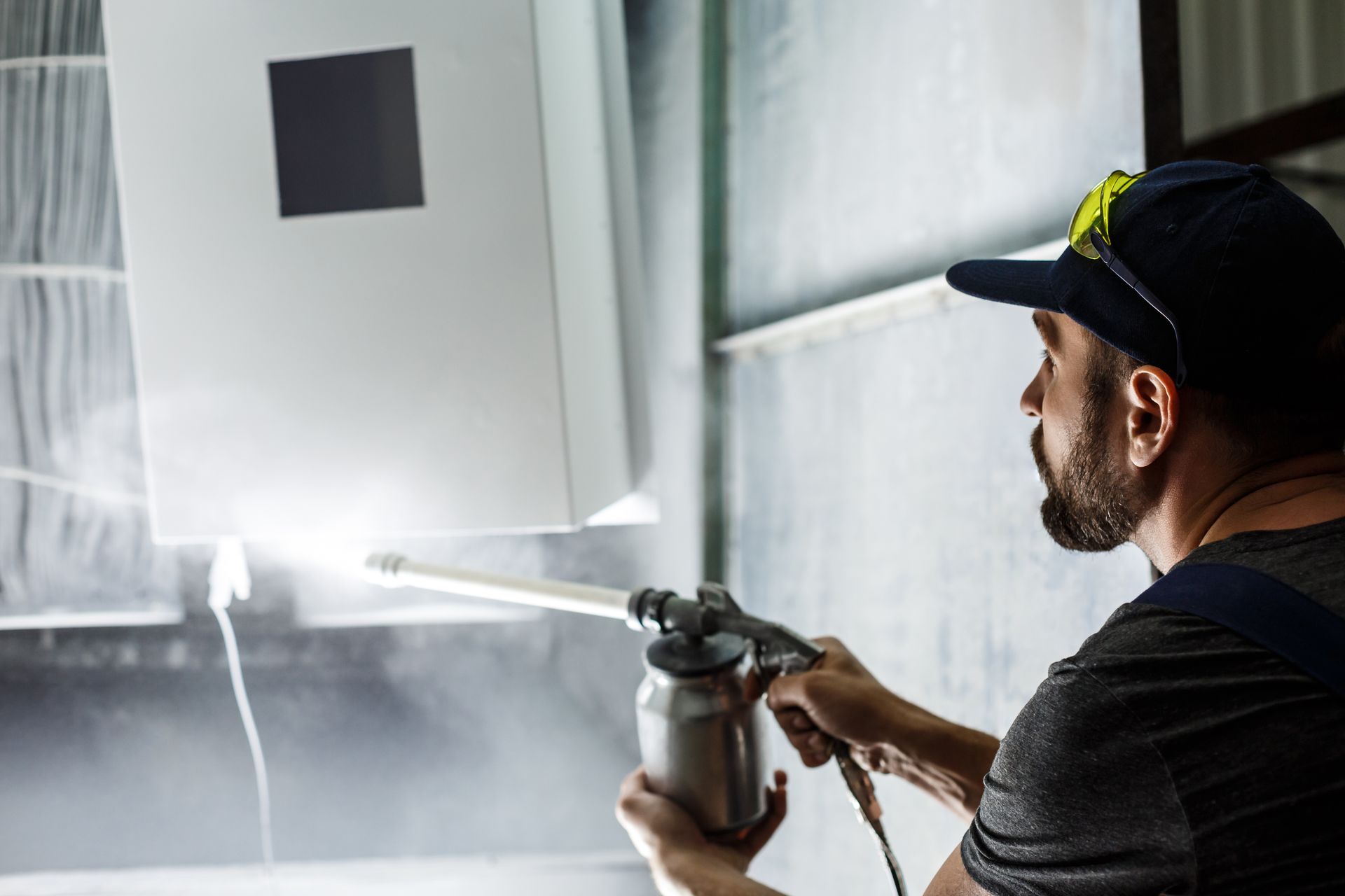 Person powder coating a metal object in a spray booth.