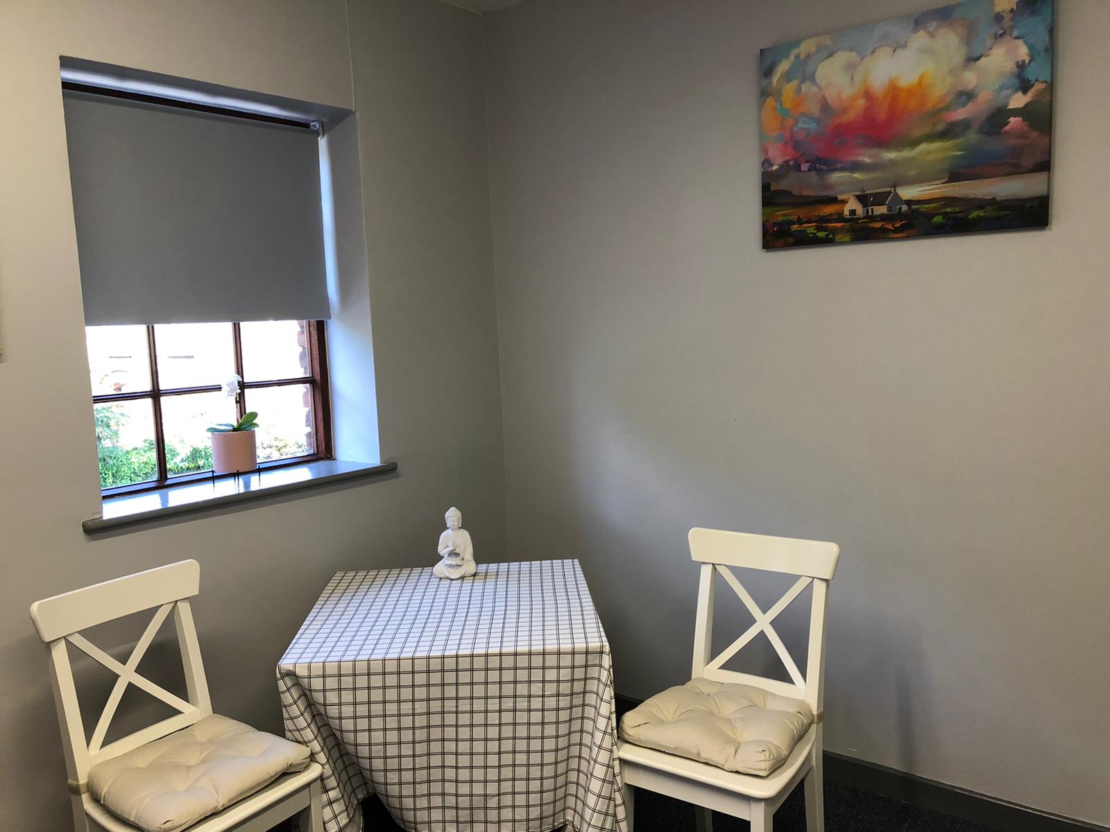 A room with a table and chairs and a painting on the wall.