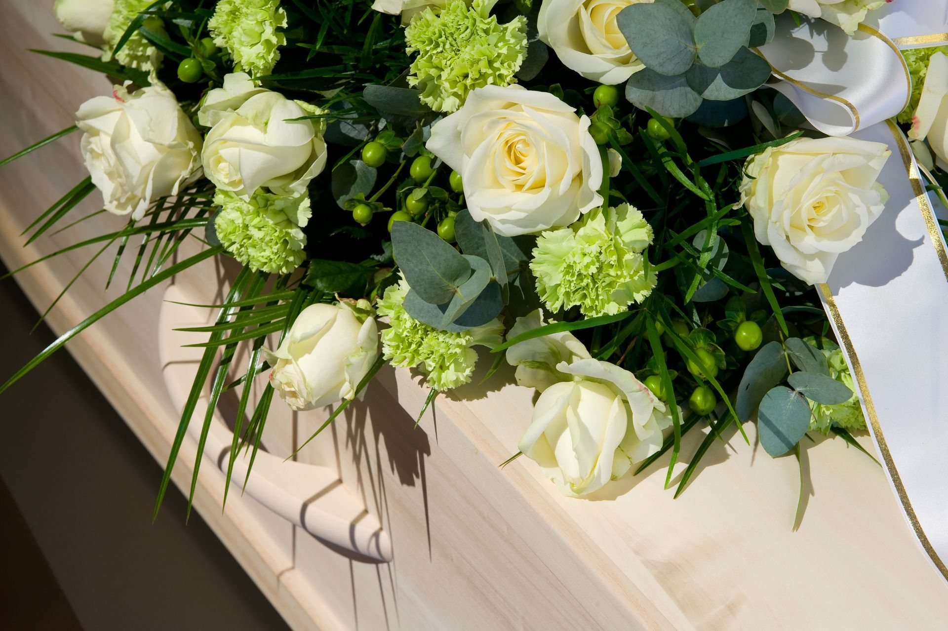 Rose bianche e fiori verdi decorano la parte superiore di una bara di legno chiaro.