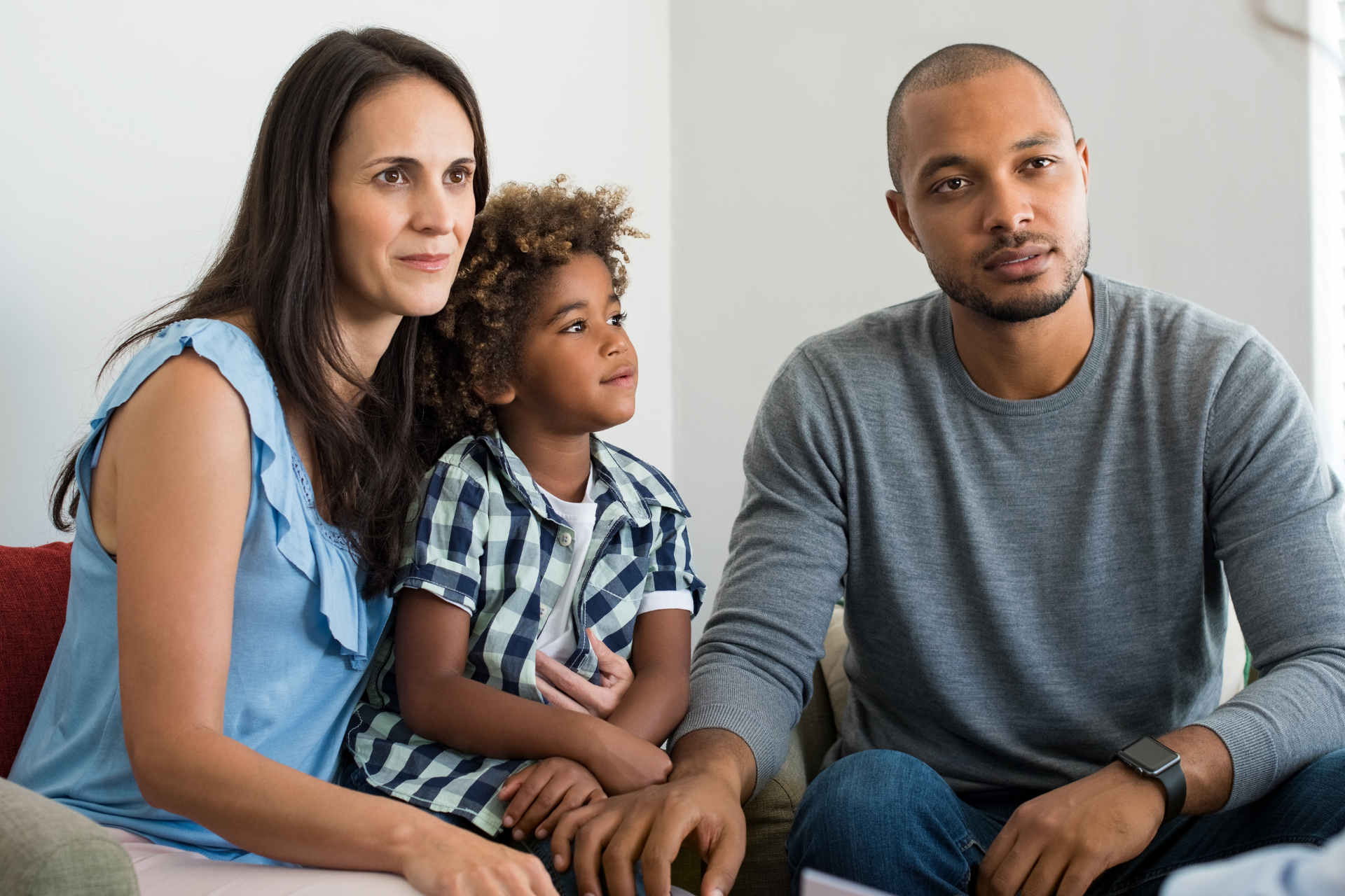 Two adults and two children sit smiling on a couch during a friendly conversation with a therapist.