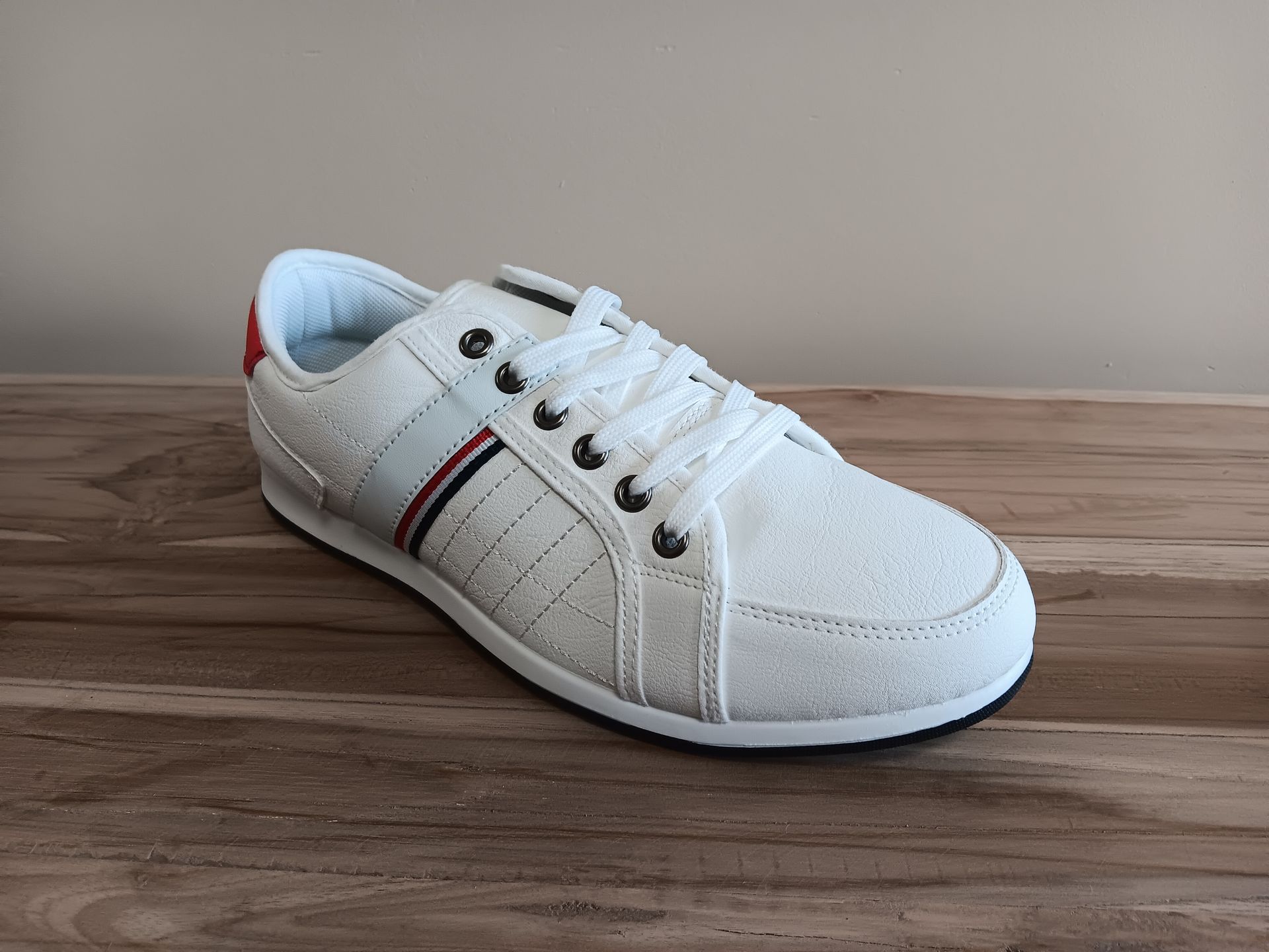 Een paar witte sneakers staan op een houten tafel.
