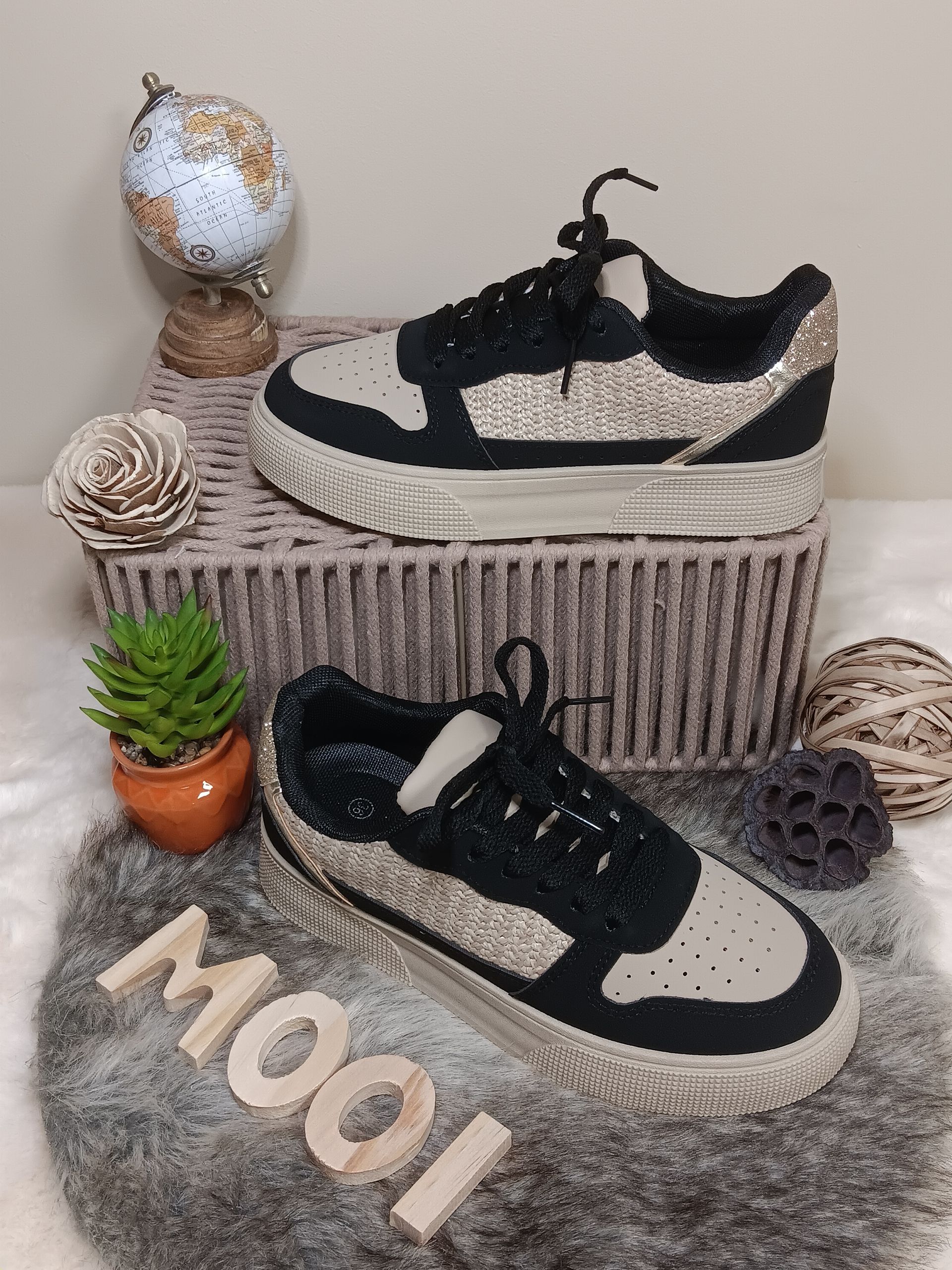 Een paar zwart-witte sneakers liggen op een kleed.