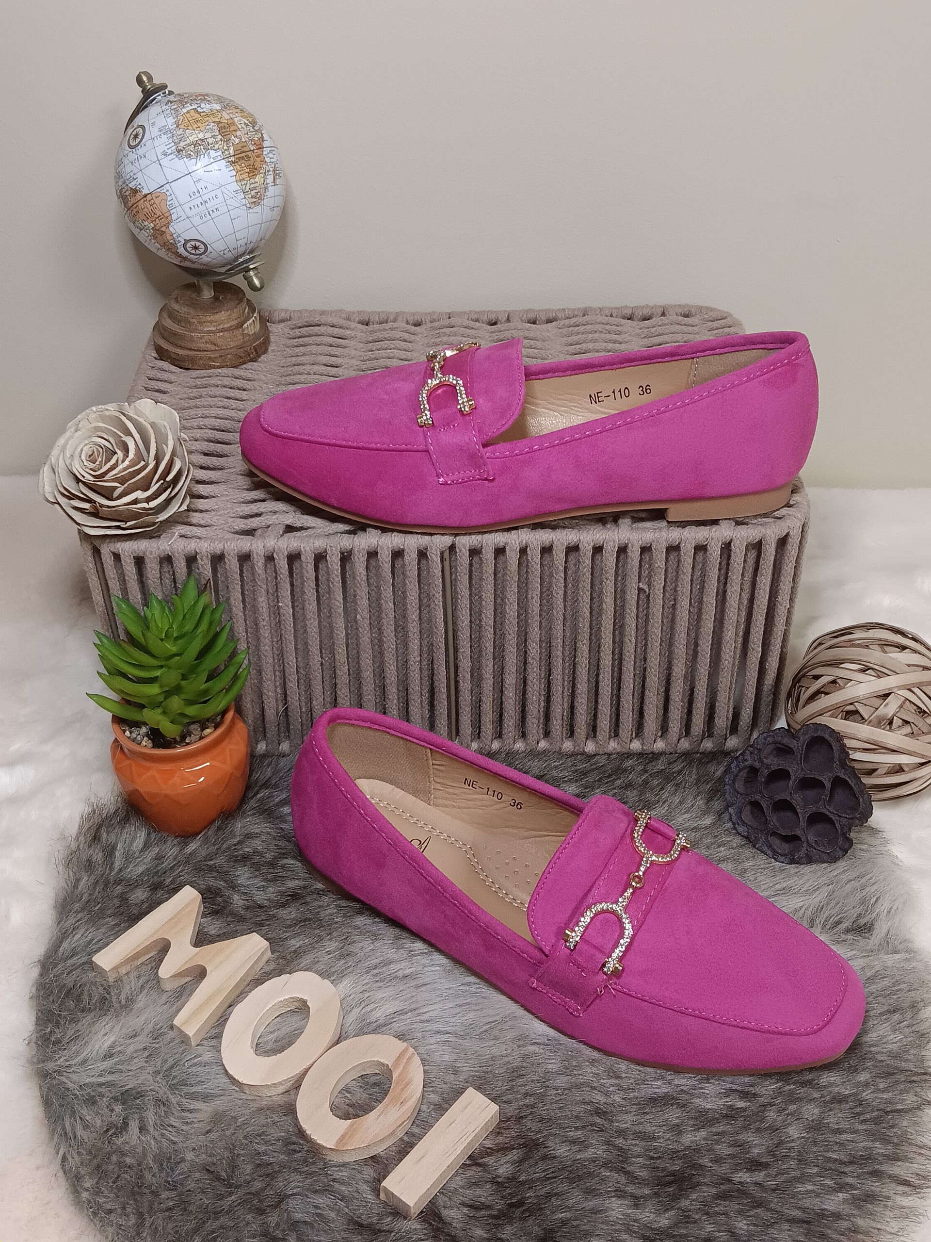 Een paar roze loafers liggen bovenop een mand.