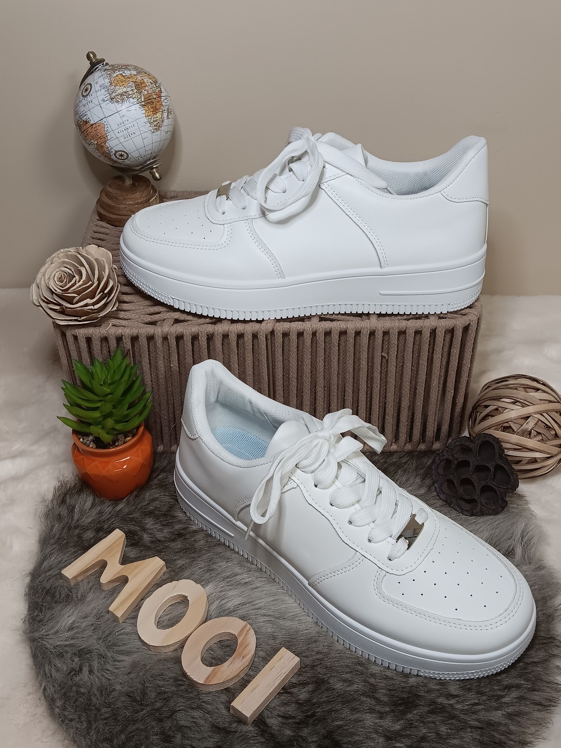 Een paar witte sneakers liggen bovenop een rieten mand.