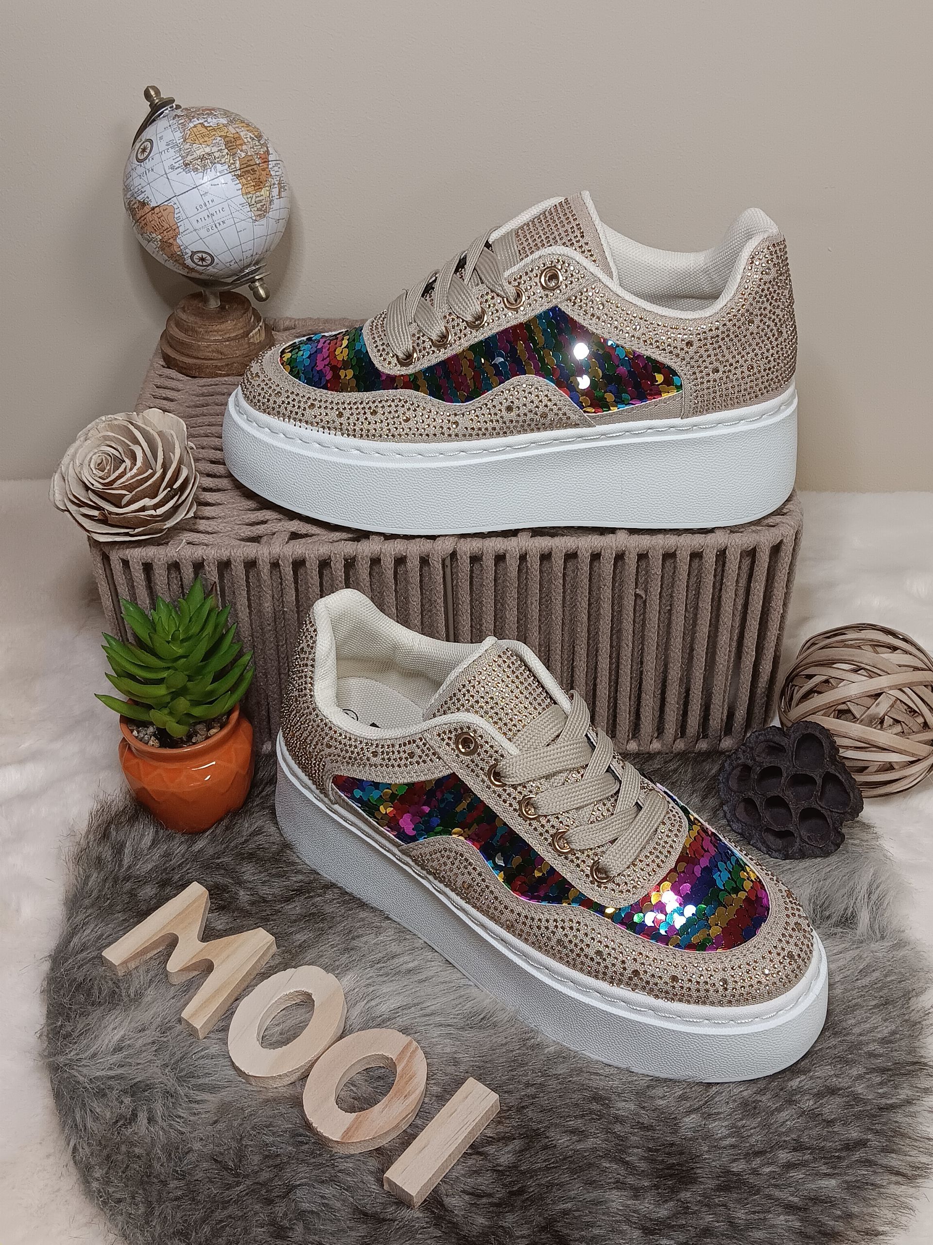 Een paar sneakers met pailletten erop liggen op een kleed.
