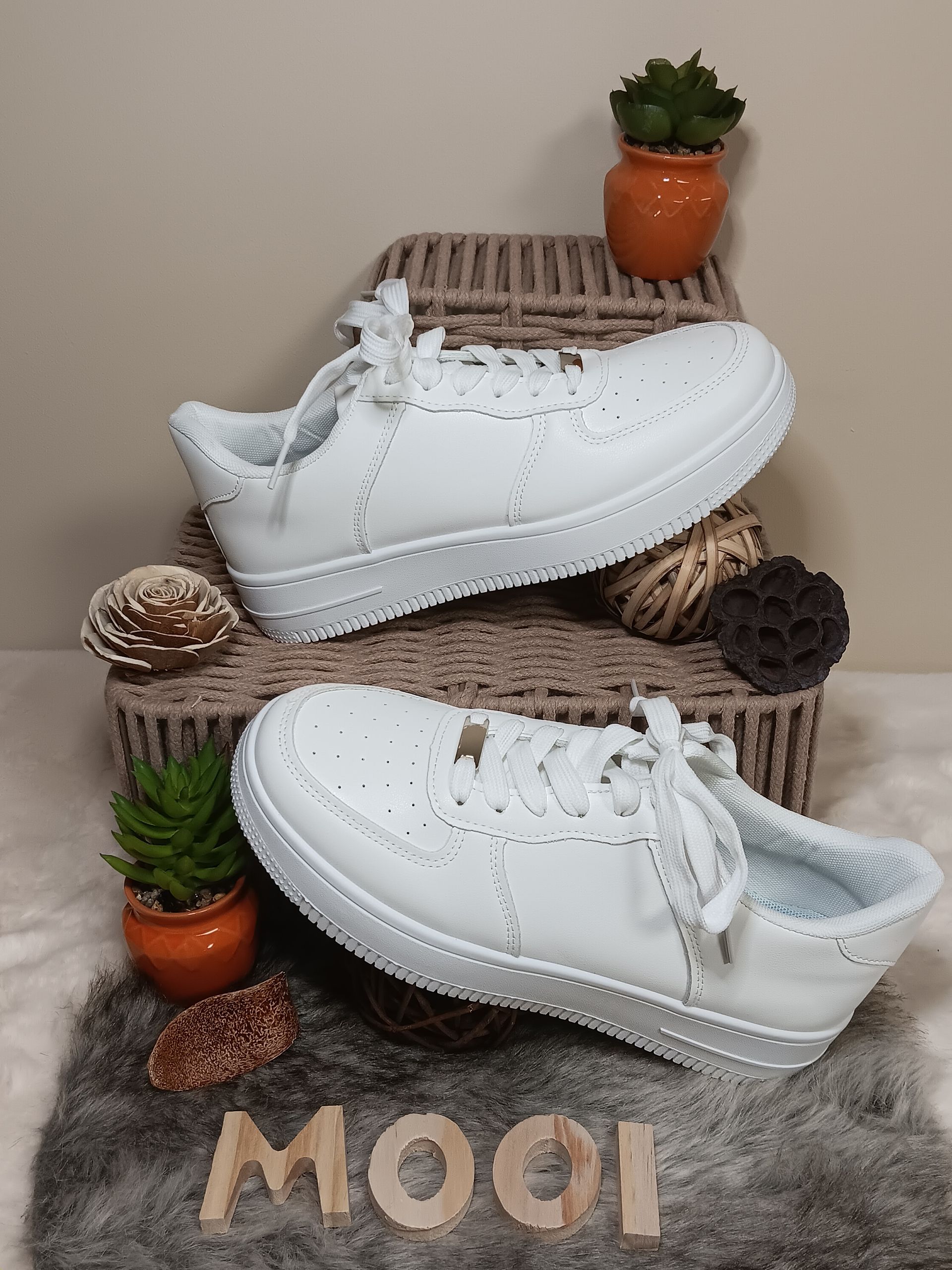 Een paar witte sneakers liggen bovenop een rieten mand.