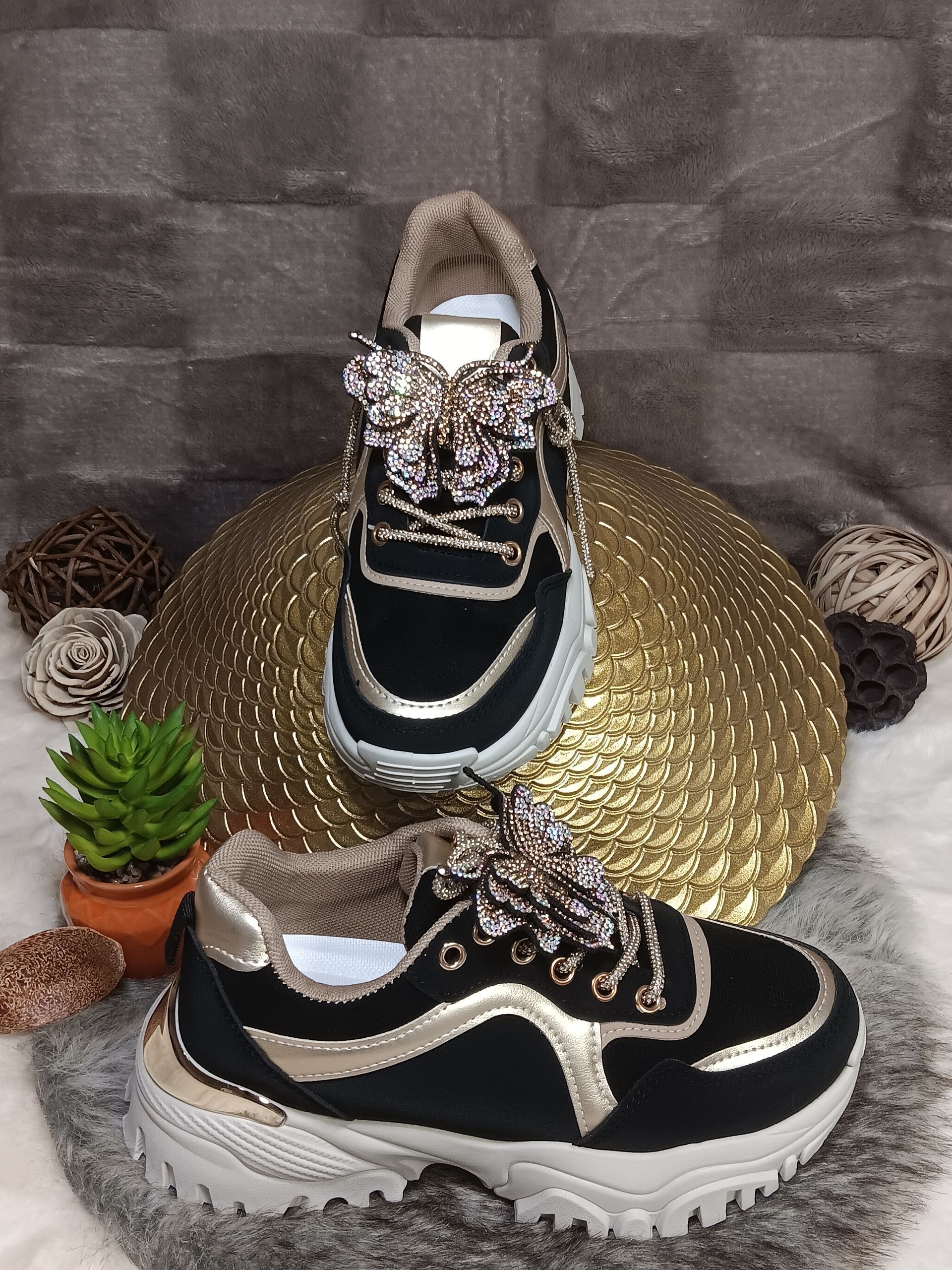 Een paar zwart-gouden sneakers liggen op een gouden plaat.