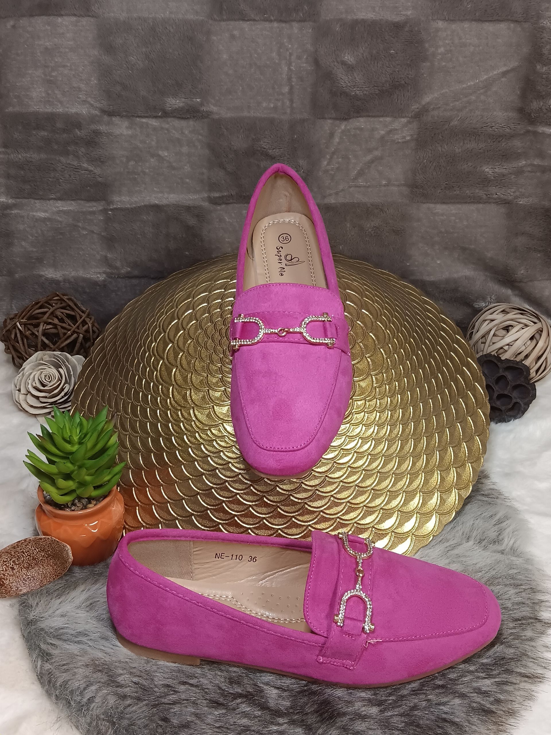 Een paar roze loafers liggen op een gouden plaat.