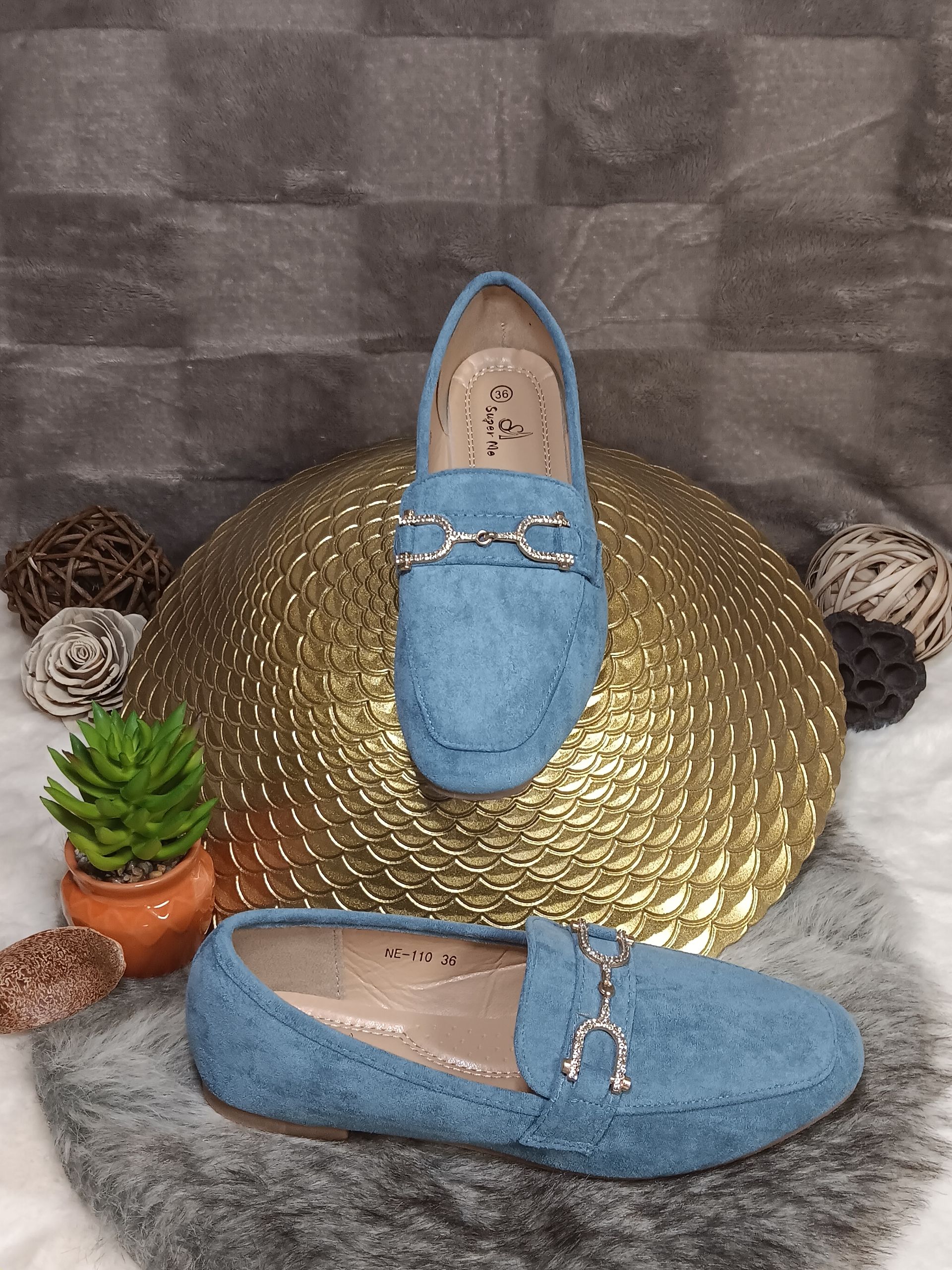 Een paar blauwe loafers liggen op een gouden plaat.