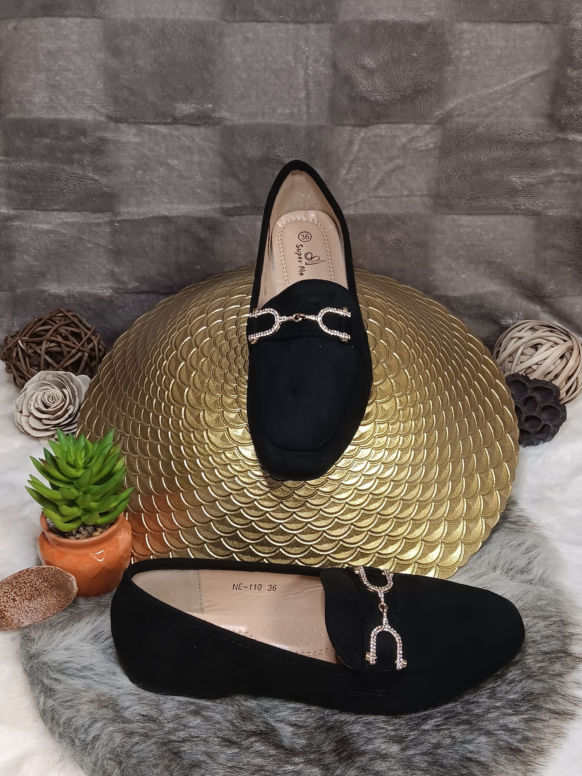 Een paar zwarte loafers liggen op een gouden plaat.