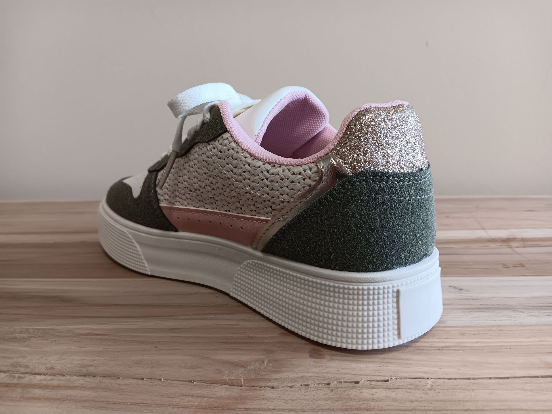 Op een houten tafel is de achterkant van een paar sneakers te zien.