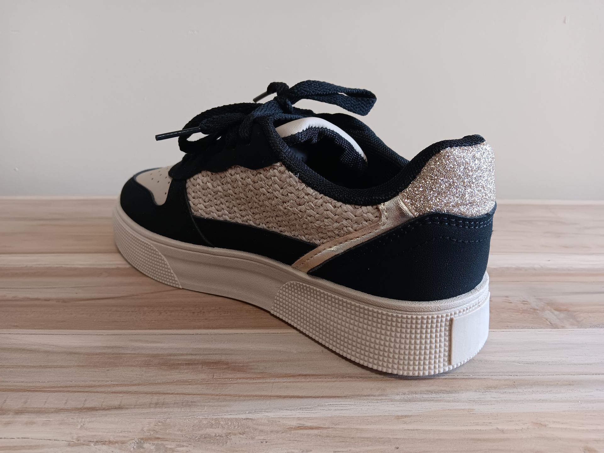 Een paar zwart-gouden sneakers staan op een houten tafel.