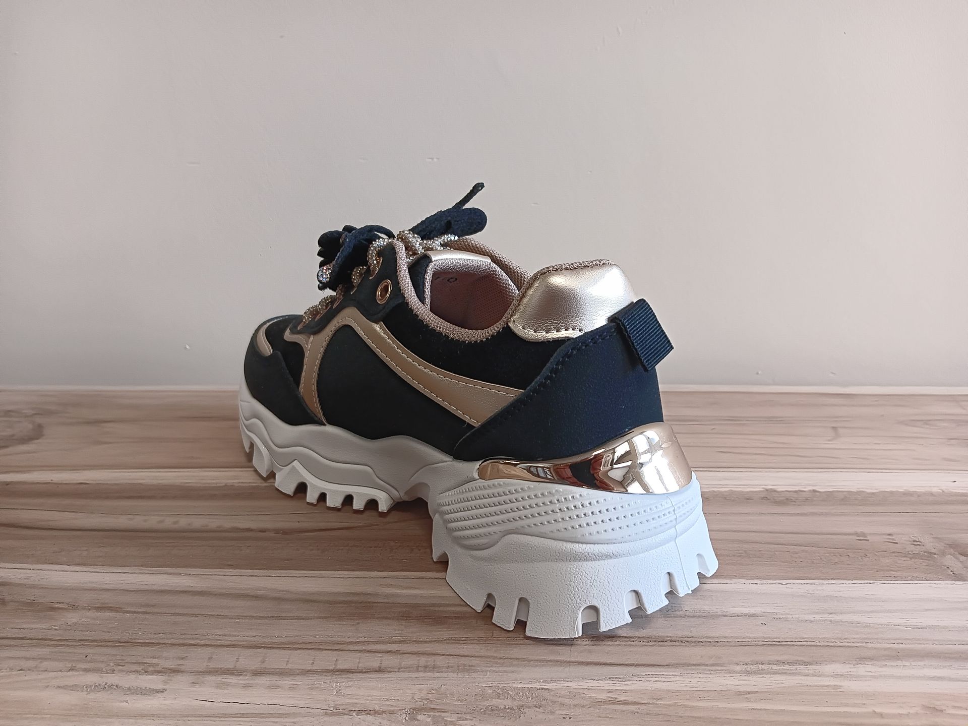 Een paar zwart-gouden sneakers staan op een houten tafel.