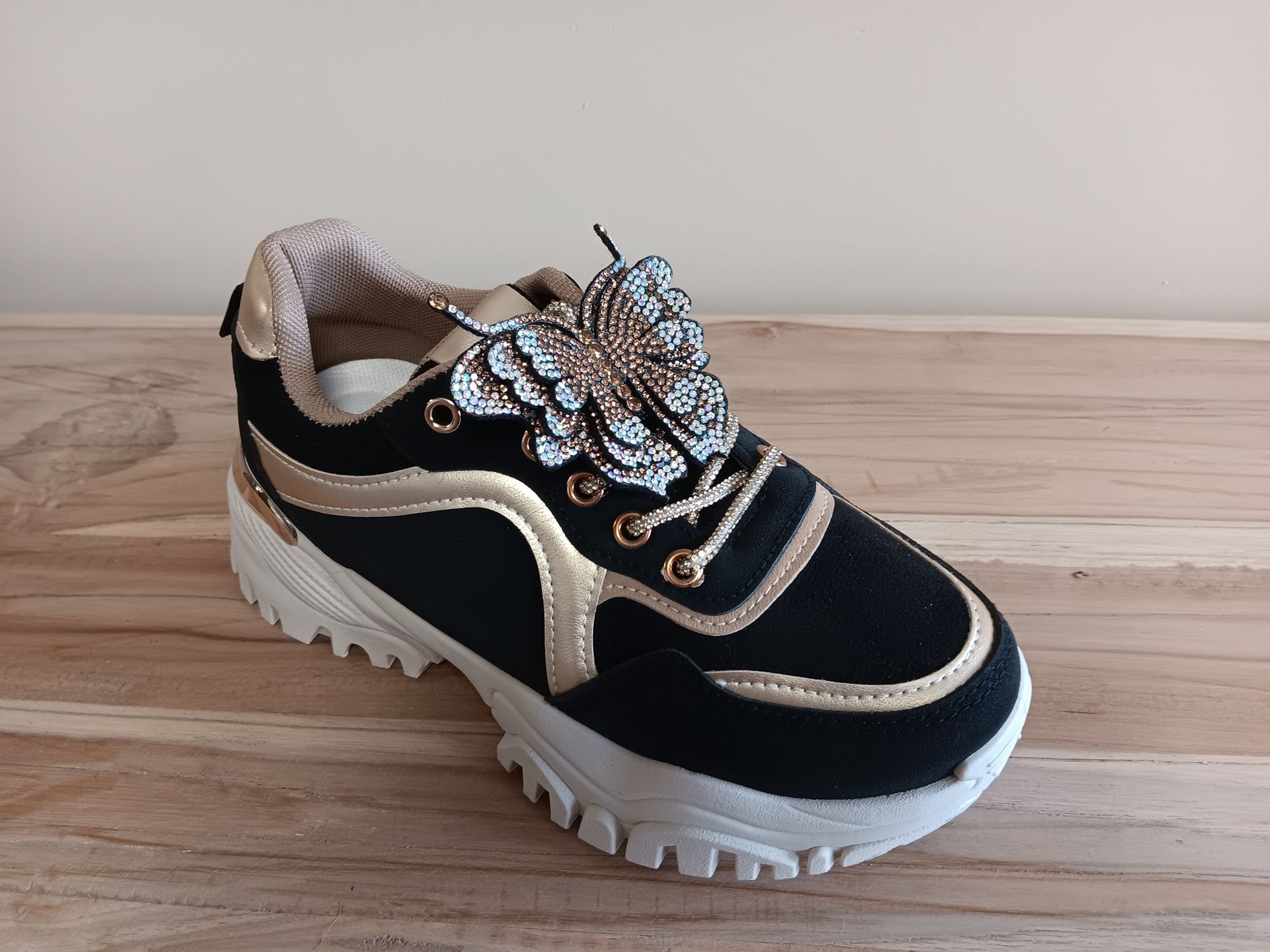 Een paar zwart-gouden sneakers staan op een houten tafel.