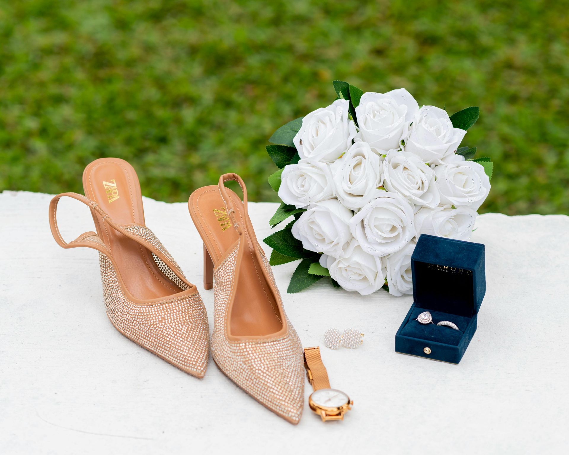 Op tafel liggen een paar schoenen, een boeket bloemen, een horloge en een ring.