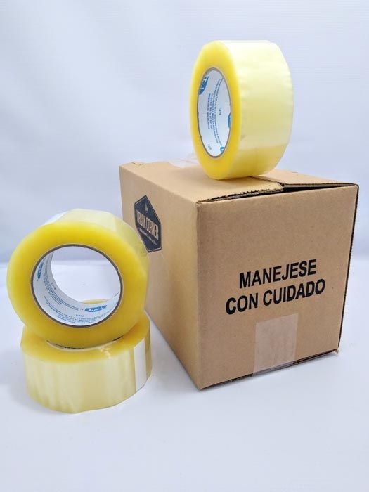 Hay dos rollos de cinta adhesiva encima de una caja que dice manejese con cuidado.