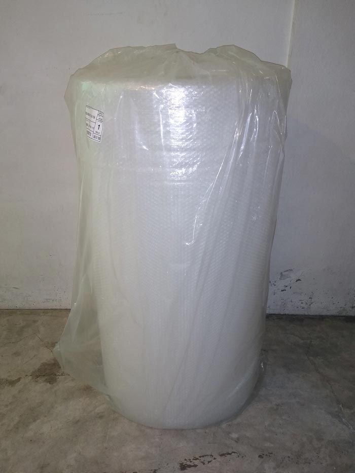 Un gran rollo de plástico de burbujas está sobre un suelo de cemento.