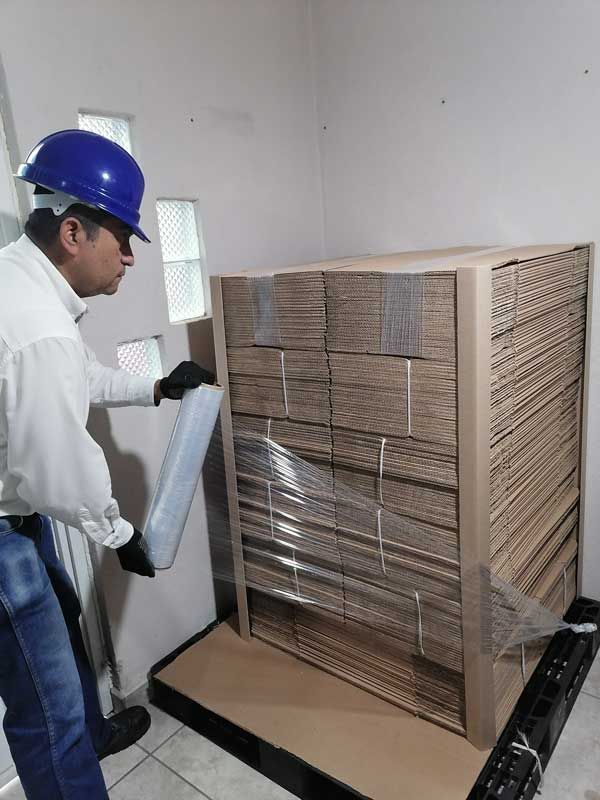 Un hombre que lleva un casco está envolviendo una caja de cartón con plástico.